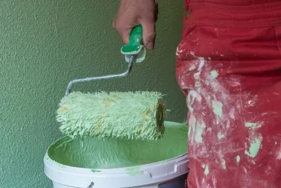 Person hält Farbrolle über Farbeimer